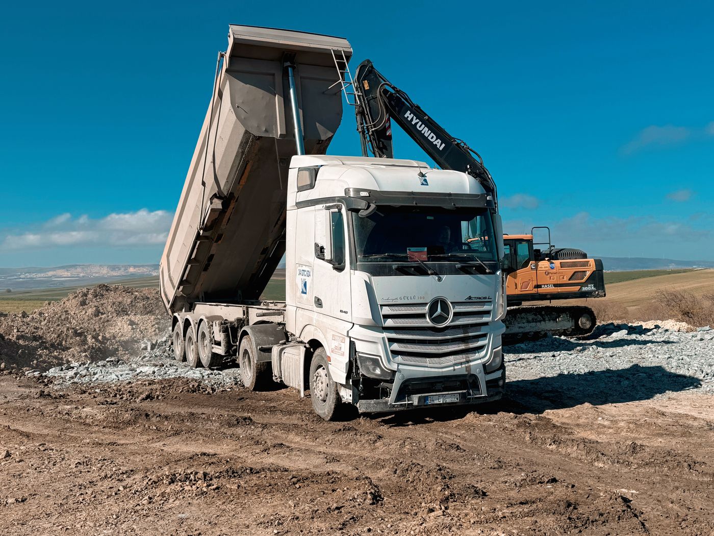 Basculantă europeană cu bena ridicată și excavator pe un șantier deschis